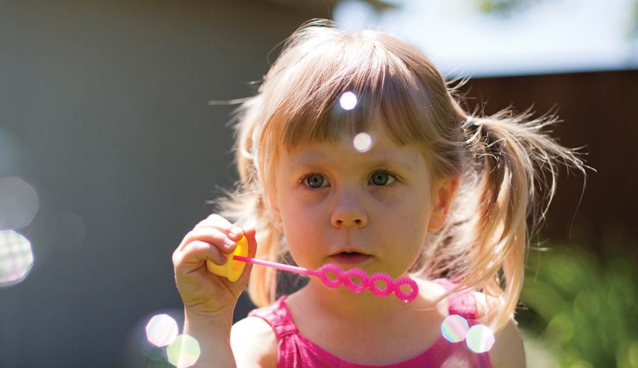Child blowing bubbles in sunlight.